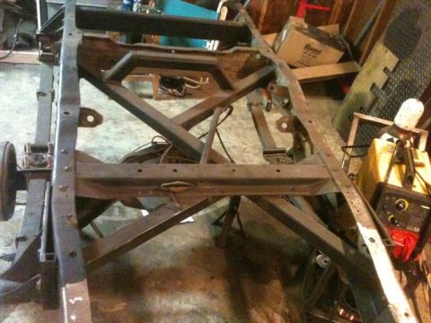 1976 Ford F-100 - The bare frame of a truck is shown in a workshop setting, with tools and equipment visible.