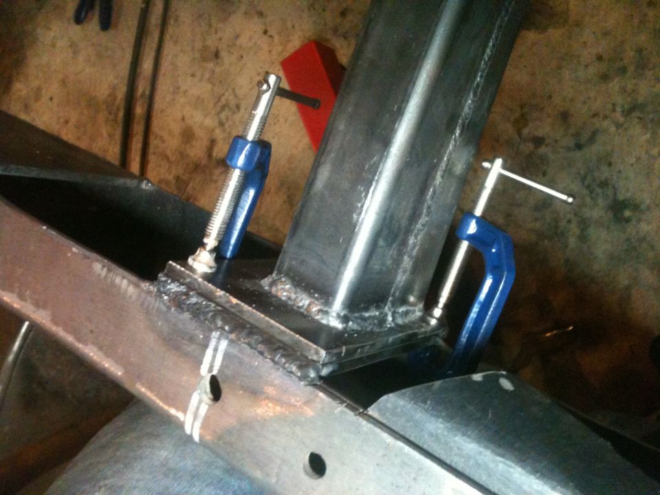 Metal frame section with two blue C-clamps holding parts together. Welds are visible