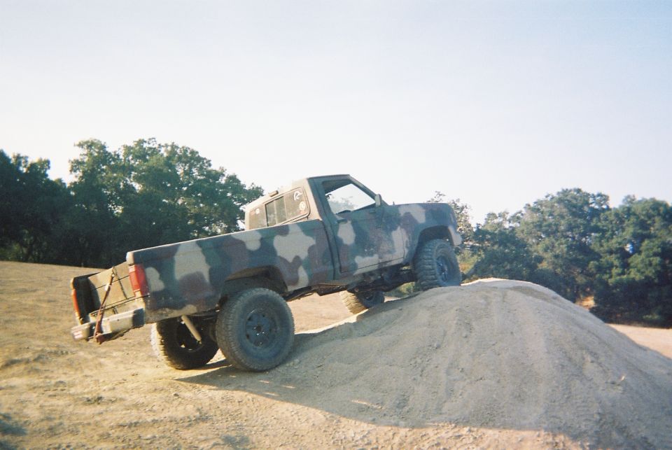Camouflaged pickup truck climbing a dirt mound, side view