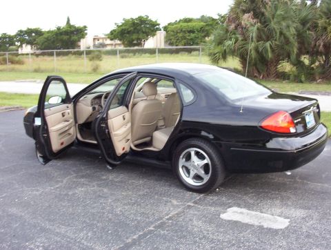2003 Ford Taurus - A black four-door Ford Taurus sedan viewed from the rear driver's side with both left doors open, revealing tan/beige cloth interior. It si…