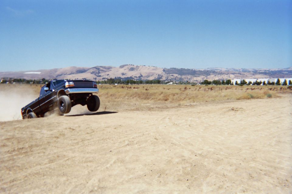 1992 Ford F-250 truck kicking up dust while driving off-road, rear-wheel lifted