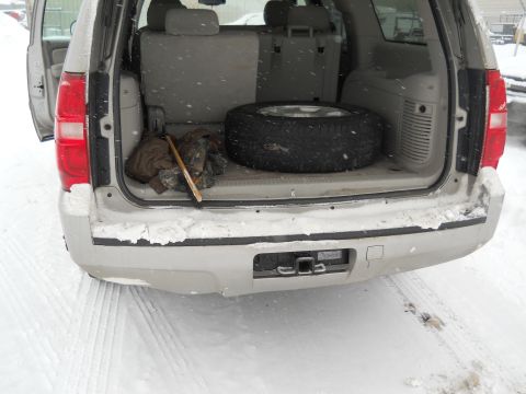2006 Ford E350 - Rear view of a silver SUV's cargo area, showing a spare tire and some tools, with snow on the ground and falling.