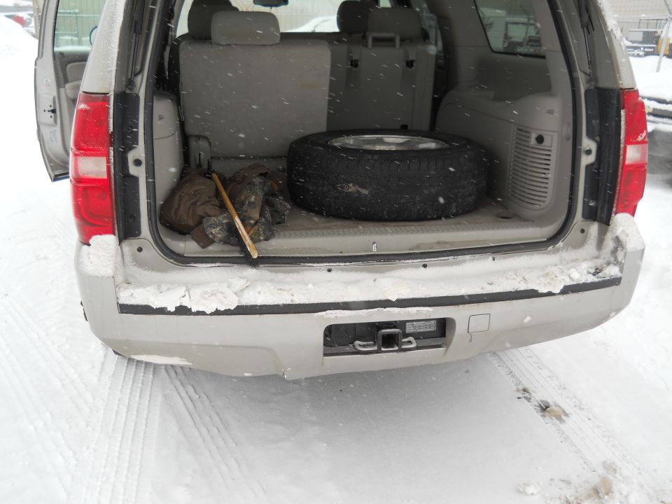 Silver SUV rear interior with spare tire and tools in snow