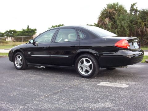 2003 Ford Taurus - A black four-door Ford Taurus sedan shown from a rear three-quarter angle in an empty parking lot, featuring five-spoke alloy wheels, a sho…