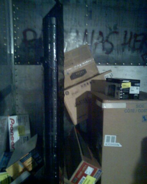 2006 Ford E350 - View inside a cargo van filled with various boxes and a tall cylindrical item, with graffiti visible on the interior wall.