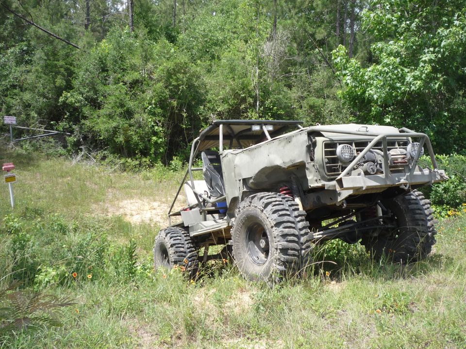 Modified off-road vehicle with large tires and roll cage, parked on grassy terrain