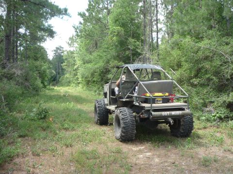 1990 Ford Bronco - This heavily modified off-road vehicle navigates a wooded trail, its large tires kicking up dust.