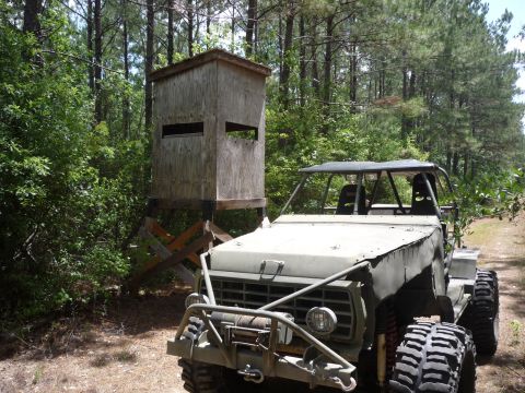 1990 Ford Bronco - This heavily modified off-road vehicle, likely from the 1980s, is parked in a wooded area next to a deer stand.