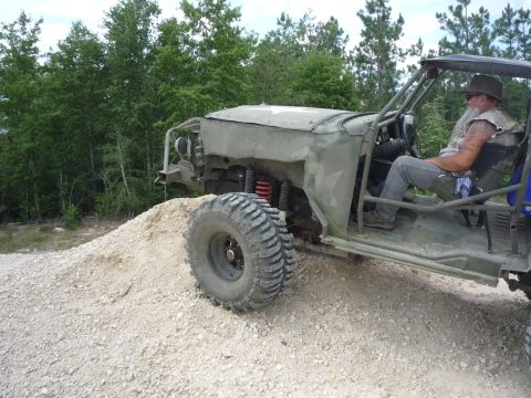 1990 Ford Bronco - Man drives a custom off-road buggy over a dirt pile in a wooded area.