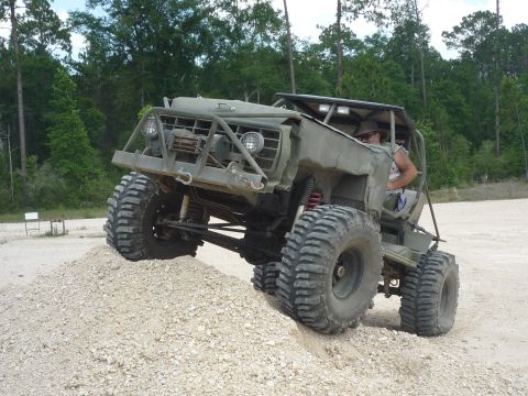 1990 Ford Bronco - A heavily modified off-road vehicle navigates a dirt incline, its large tires gripping the loose surface.