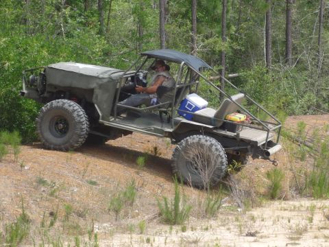 1990 Ford Bronco - A man drives a heavily modified, open-air vehicle through a wooded, off-road area.