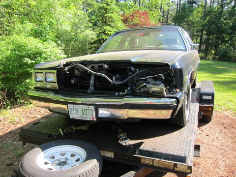 1991 Ford Crown Victoria LTD - A 1991 Ford Crown Victoria LTD is seen on a trailer with its front end heavily damaged, revealing the engine components.