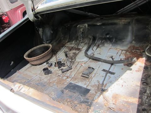 1991 Ford LTD Crown Victoria - The interior of a car trunk shows significant rust and debris, with a spare tire well and various disconnected components.