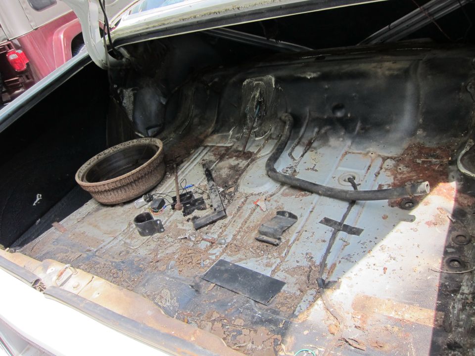 Car trunk interior with rusty floor, spare tire well, and loose parts