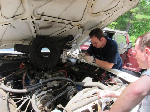 1991 Ford LTD Crown Victoria - Two men work on the engine of a white 1991 Ford Crown Victoria LTD, with a red Jeep visible in the background.