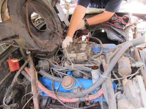 1991 Ford LTD Crown Victoria - Mechanic's hands in white gloves work on the carburetor in a cluttered engine bay with a blue engine block.