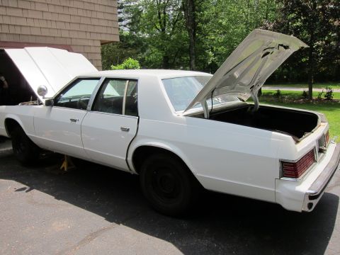 1991 Ford LTD Crown Victoria - White sedan with hood and trunk open, parked outside a building.
