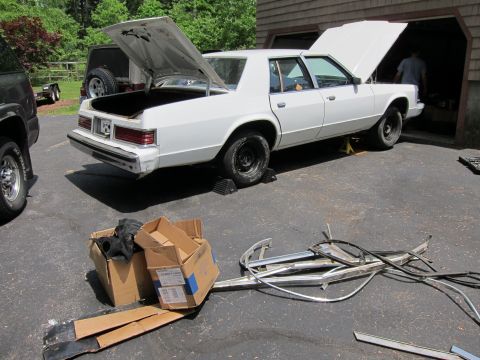 1991 Ford LTD Crown Victoria - A white sedan is parked in a driveway with its hood and trunk open, surrounded by car parts.