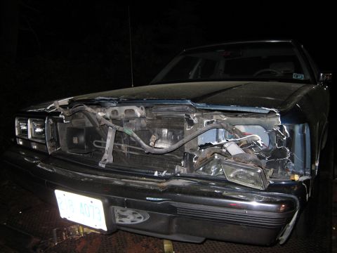1991 Ford LTD Crown Victoria - The front of a car is severely damaged, with the hood open and parts of the engine exposed.