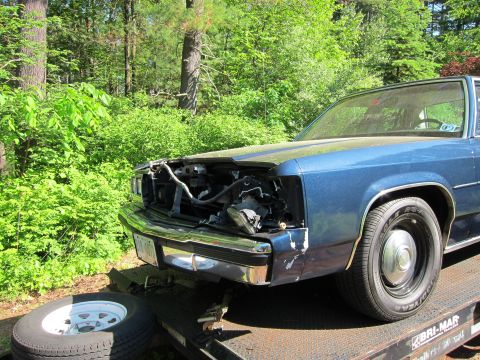 1991 Ford LTD Crown Victoria - A blue sedan with a damaged front end is loaded onto a trailer.