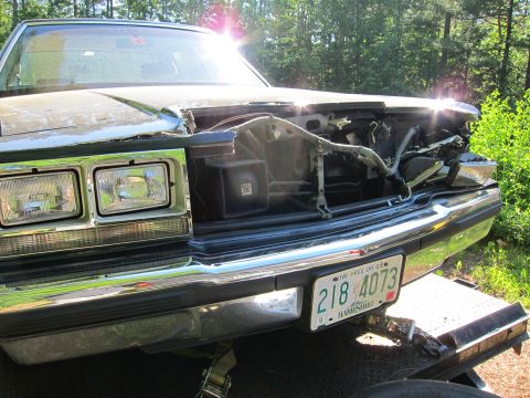 1991 Ford LTD Crown Victoria - A dark sedan with a damaged front end is parked outdoors, showing its grille and headlights.