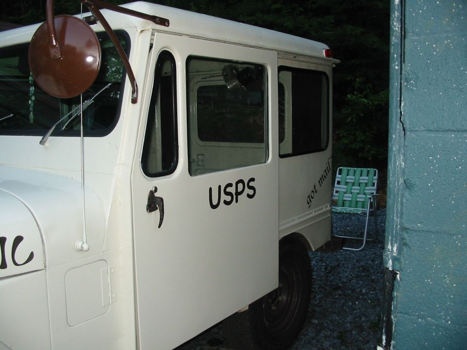 White USPS delivery truck parked next to a building, showing the side door with 'USPS' and 'got mail' text