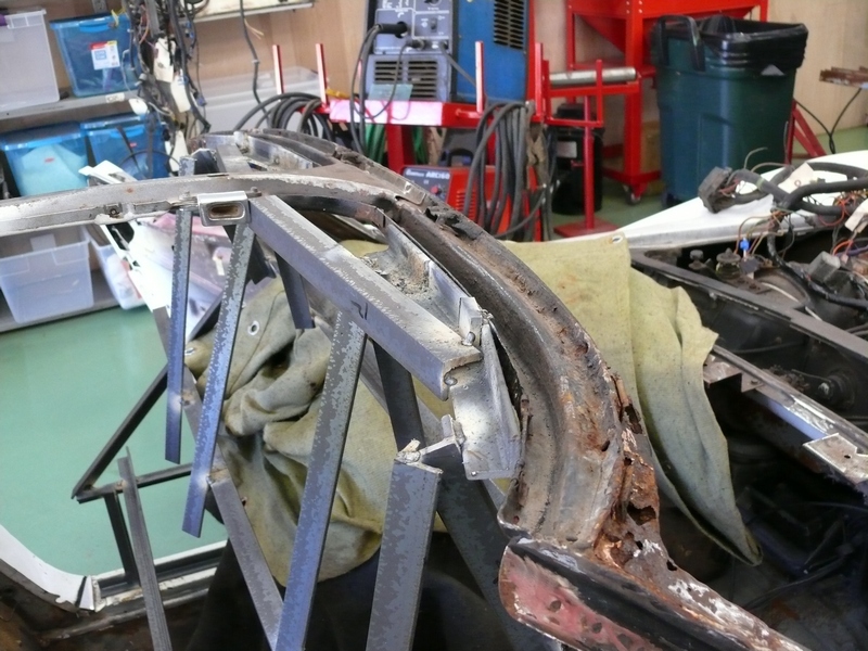 Car frame with rust and metal supports, showing interior wiring and a green trash can in the background