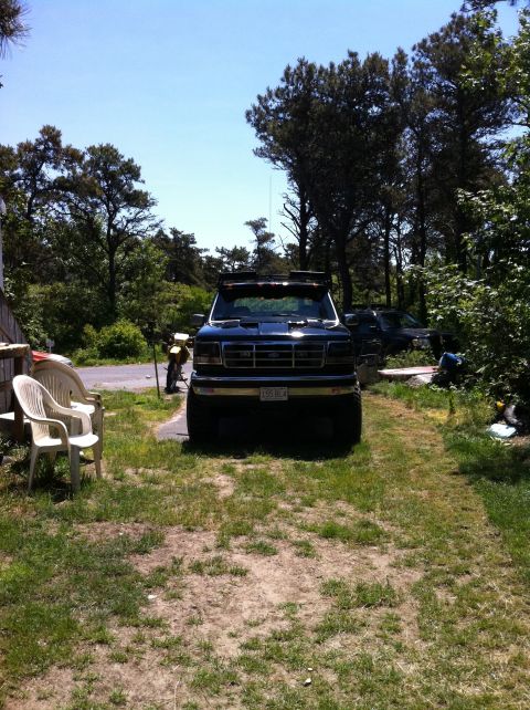 1993 Ford Bronco - This lifted pickup truck features a prominent grille and aftermarket lighting on its roof, with another vehicle visible in the background.