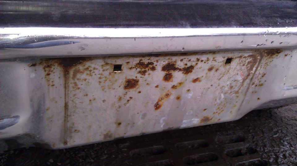 Rusted rear bumper with chrome trim and license plate holes