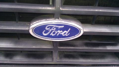 1984 Ford Bronco - The blue Ford oval emblem is centered on the horizontal bars of the vehicle's grille.