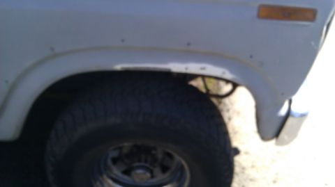 1984 Ford Bronco - Detail of a vehicle's front fender and tire, with visible rust near the wheel opening.