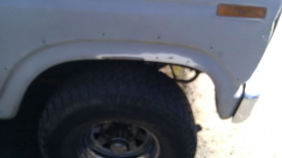 Gray 1980s SUV fender with visible rust spots and a large tire