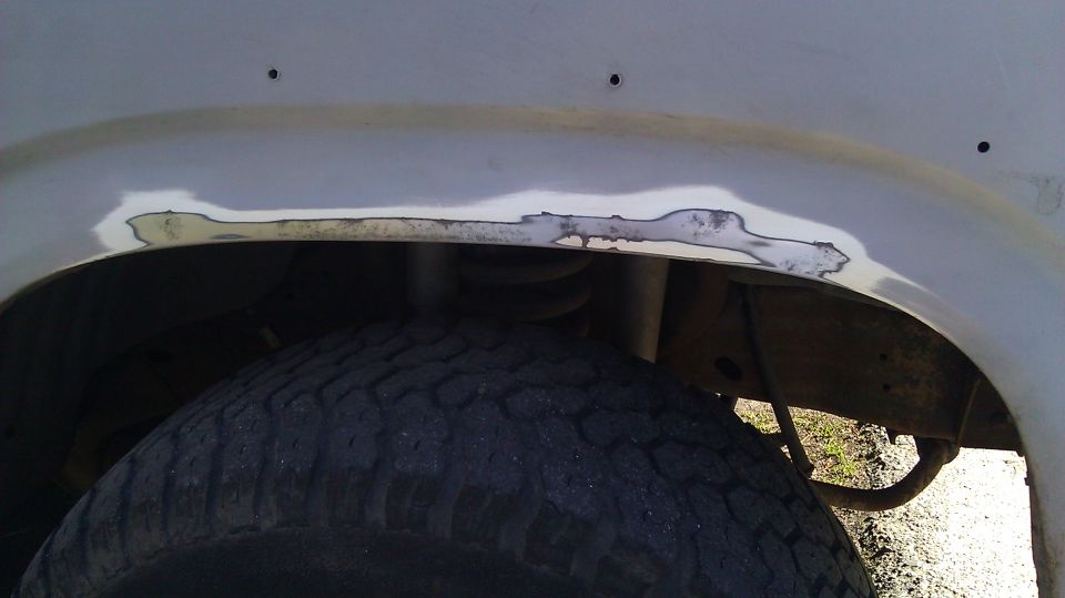 Close-up of body filler on a vehicle's rear wheel well, showing rust repair