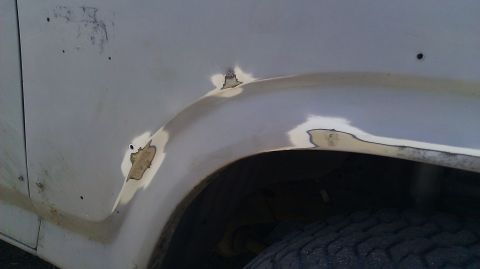 1984 Ford Bronco - Close-up view of rust damage and primer on a vehicle's fender, indicating repair work.