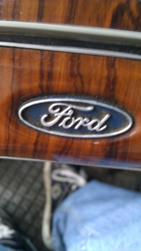 1984 Ford Bronco - Close-up of a Ford emblem on wood grain trim inside a vehicle.