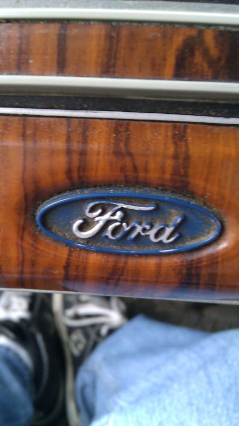 1984 Ford Bronco - Close-up of a Ford logo on wood grain trim, likely from a vehicle's interior.