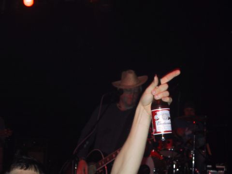 1989 Ford Bronco - A person holds up a Budweiser bottle while a band performs on stage in the dimly lit venue.