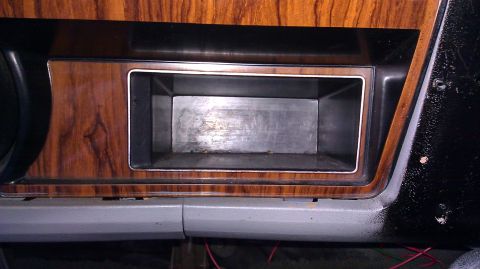 1984 Ford Bronco - Close-up of an empty dashboard compartment with faux wood paneling.