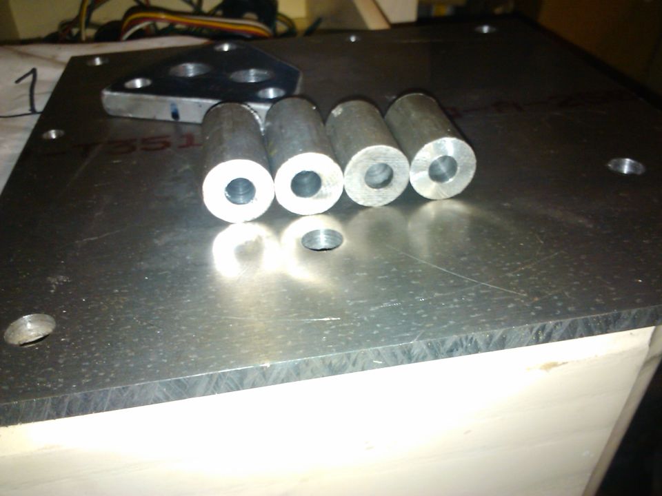 Four metal cylinders and a metal bracket sit on a large metal plate. Text is visible on the plate