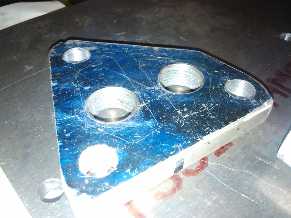 Blue metal bracket with three bolt holes and two larger holes, scratched surface, on a metal plate