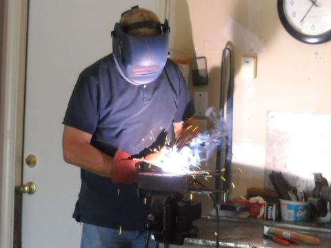 1986 Ford Bronco II - A person is welding metal in a workshop setting, with a clock on the wall and various tools visible.