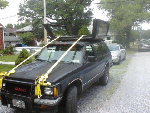 1988 Ford Bronco - A dark blue GMC SUV is shown with its roof removed and secured to the roof rack with straps.