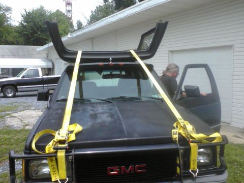 1988 Ford Bronco - A black GMC truck is being loaded with a roof rack part secured by yellow straps.