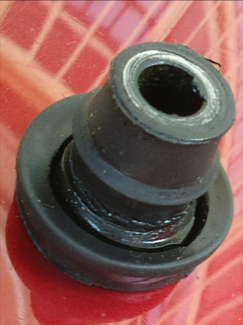 1998 Ford Crown Victoria - A close-up view of a black rubber valve cover grommet with a metal insert, resting on a red surface.