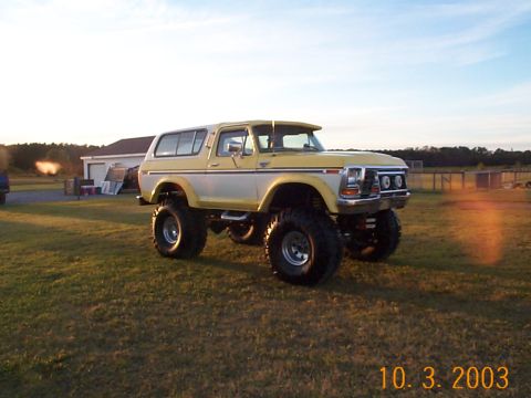 1978 Ford Bronco - Modified 1978 Ford Bronco with custom two-tone paint and lifted suspension sits in a grassy field at sunset.