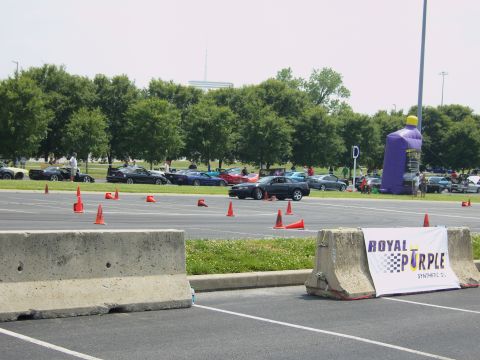 2007 Ford Mustang - A dark 2007 Ford Mustang navigates a course marked by orange cones, with a large inflatable bottle and sponsor banner visible in the backgr…