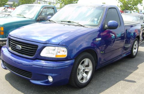 2007 Ford Mustang - A blue Ford F-150 Lightning pickup truck is parked next to another truck.