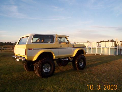 1978 Ford Bronco - A two-tone SUV with large tires sits on a grassy field under a clear sky.