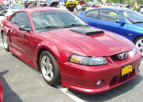 2007 Ford Mustang - A red Ford Mustang is parked at an outdoor car show, with other vehicles and tents in the background.