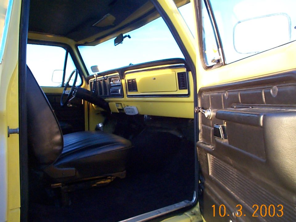 Interior of a late-1970s Ford truck with black bench seat and yellow dash, passenger door open